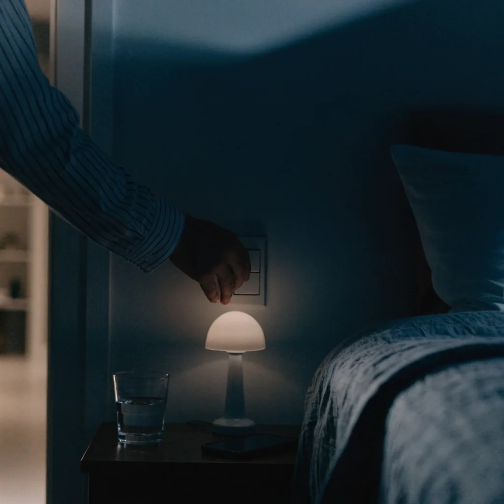 A dark bedroom at night with a made bed, water glass and a phone placed face down