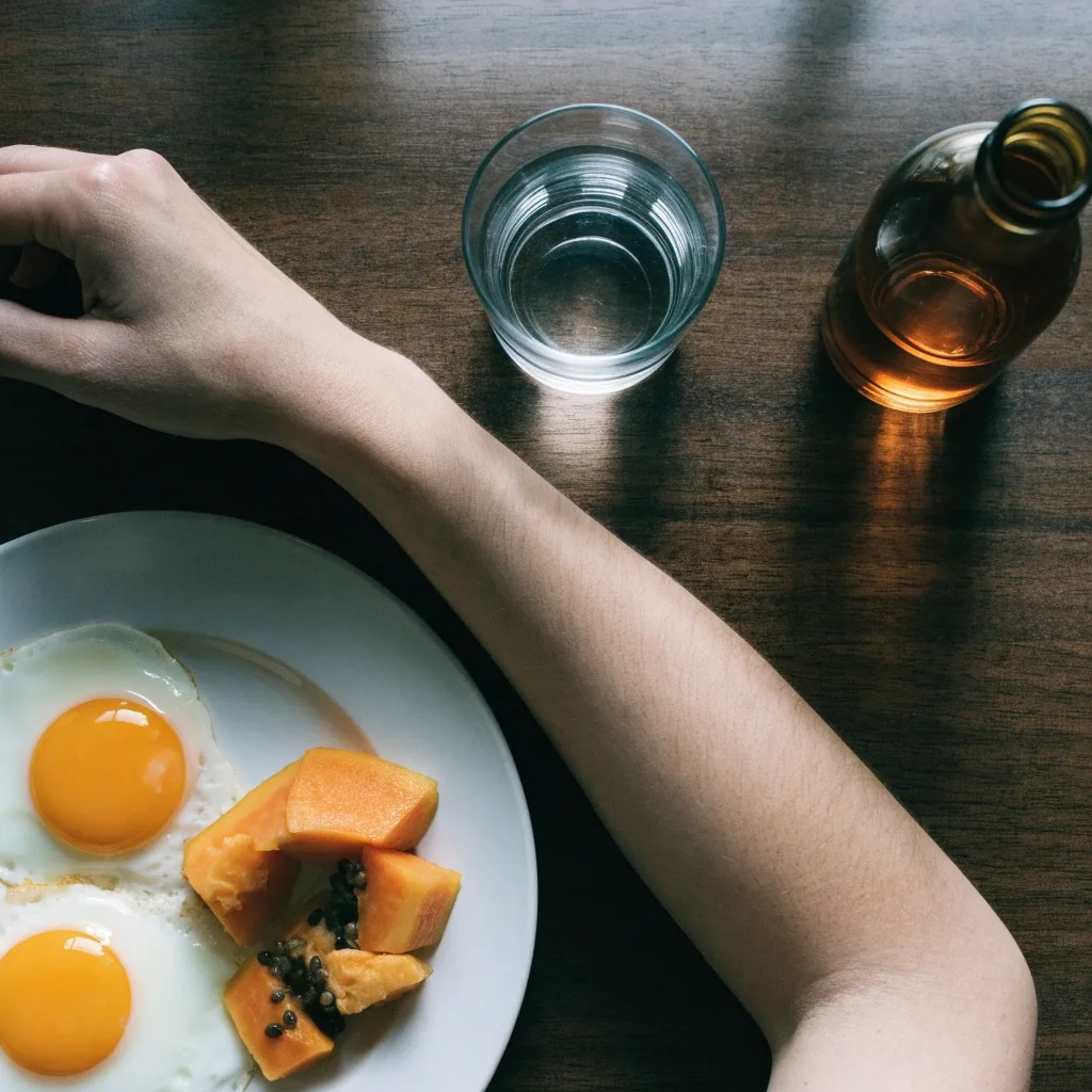 A breakfast plate with eggs, fruit, a glass of water and an unlabelled bottle on a dark counter