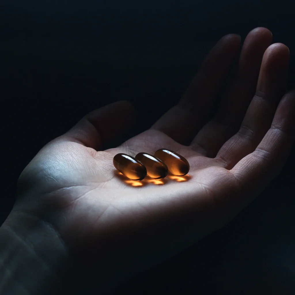An open hand holding three amber softgel capsules under night lighting